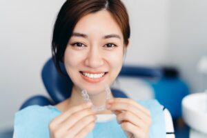 Smiling Asian woman holding a dental aligner 